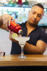A man is pouring a drink into a glass with a lime wedge in it