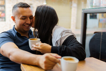 A man and woman are kissing each other while holding cups of coffee