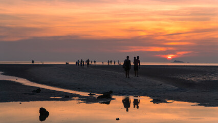 Group walking on beach during sunset, admiring red sky at dusk over water