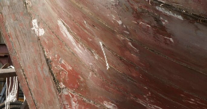 close up of a worker cleans out the hull of a fishing boat, then cuts a piece of white string and uses it to plug a hole.