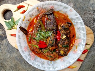 Mangut lele placed in a plate isolated on cement floor background. Dish made from fried catfish, chili, basil, coconut milk and some spices. Yogyakarta traditional dish. Indonesian food.