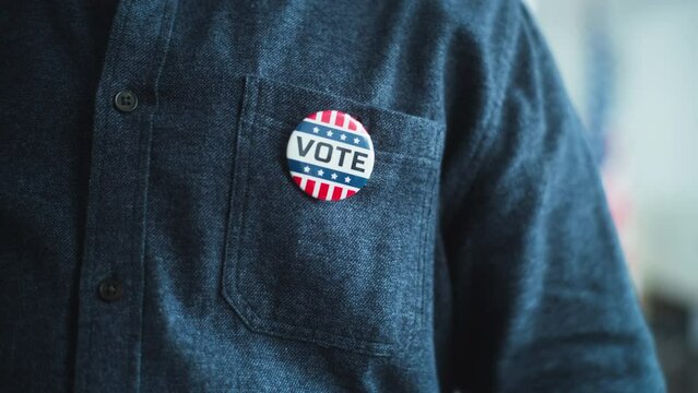 Close up of anonymous African American man or US citizen putting on badge with USA flag logo and inscription I Voted. Male voter at polling station after voting. Election Day in the United States.