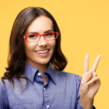Happy smiling beautiful business woman in red glasses showing two fingers or victory hand v-sign gesture, isolated over orange yellow background. Square image