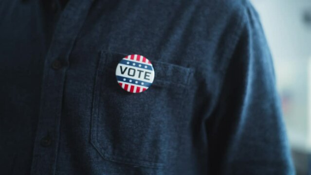 Anonymous African American man puts on badge with USA flag logo and inscription I Voted. US citizen at polling station during elections. National Election Day in United States of America. Close up.