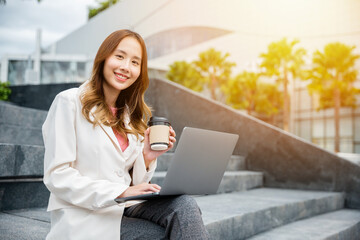 Attractive girl using laptop computer outdoors. City street and coffee cup in the background make a perfect summer scene. Ideal for remote work, entrepreneurship or online lifestyle themes.
