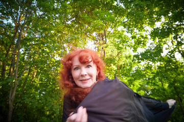 Elegant senior mature Woman dancing in Black Dress in green park. Woman with red hair posing on nature landscape