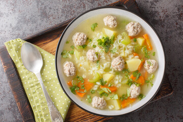 Dietary Rice meatball soup with celery, carrots, onions, potatoes and herbs close-up in a bowl on the table. Horizontal top view from above