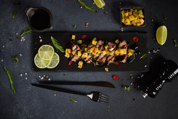 Sliced Organic grilled Tuna fillet covered with sesame seeds and mango salsa on black stone serving board