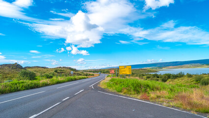 Panoramic over paved Ring road near Egilsstadir in Iceland with beautiful green landscape, lake and blue sky. Information board sign with distances to major cities.