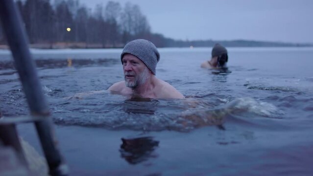 An ice bathing couple in their 50s, the man swims back to the pontoon