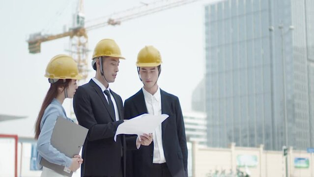 Architect And Inspector In Helmets With Documents Checking Plans At Construction Site. Contractor recheck drawing and solve building structure problems.