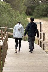 A man and woman are walking on a wooden bridge - rear view