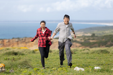 A couple running on a grassy hill overlooking the ocean