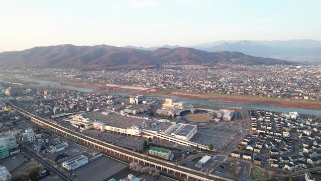 Expansive aerial view at twilight of Ueda city with a train station, river, and mountains in the distance.