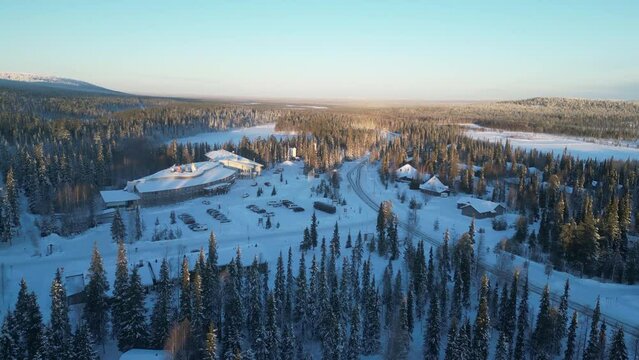 Aerial drone footage of Luosto, Finland, in Lapland the Arctic Circle during winter. Don captures a 180-degree turn over the snowy town, showcasing the hotel, shops, trees, and roads at -20°C i