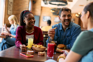 Young happy man and his friends talking while eating in  pub.