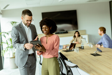 Joyful colleagues sharing a laugh over a tablet in a modern office meeting room