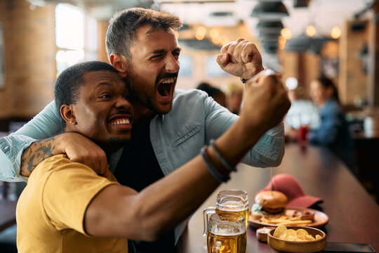 Excited men cheering while watching watching sports game on TV in  bar