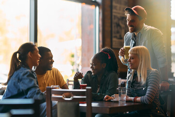 Young happy friends talking while having  drink in  pub. - obrazy, fototapety, plakaty