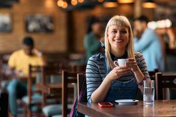 Happy woman enjoying in cup of coffee in  cafe and looking at camera.