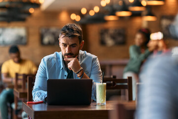 Pensive man using laptop while sitting in  cafe.