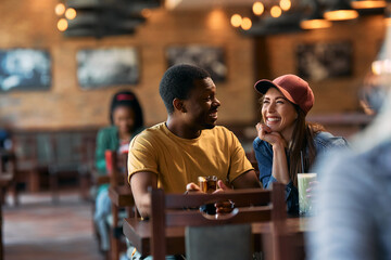 Happy multiracial couple having fun while talking in pub. Copy space.