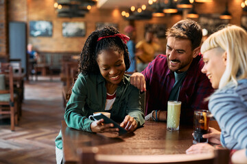 Young happy friends using smart phone in pub.