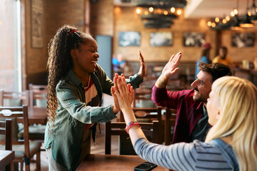 Group of happy friends giving high-five while gathering in pub.