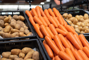 A mountain of carrots next to potatoes in the vegetable section of a grocery store.
