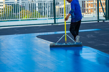 Fototapeta na wymiar Workers Spreading floor paiting with Squeegee , Tennis court and sport floor painting by squeegee