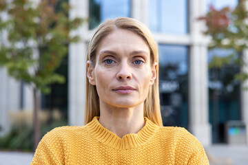 Close-up portrait of a confident middle-aged woman wearing a yellow sweater, standing outdoors with...