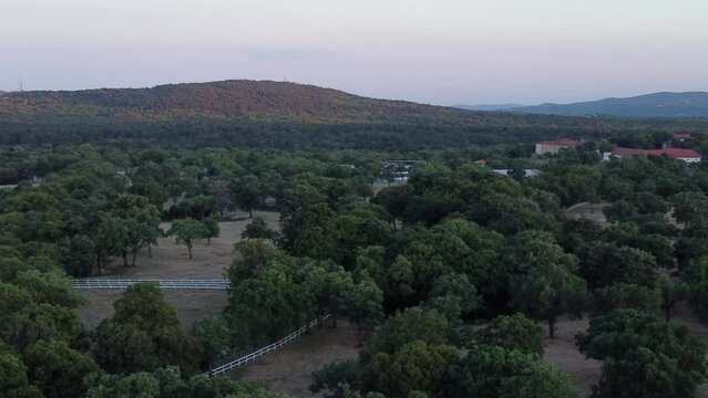 Drone ascends revealing the verdant expanse of Lipica Stud Farm against a dusk sky in Slovenia.