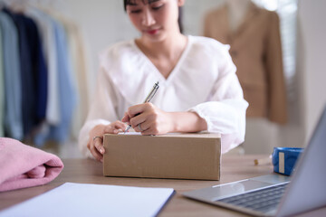 Young asian merchant women writing address data in cardboard box and preparing to shipping delivery customer while checking purchase online order on laptop and working about online shopping business