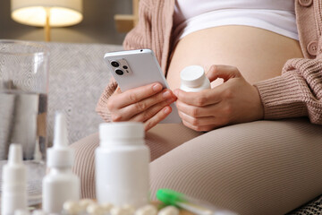 Obraz na płótnie Canvas Unrecognizable anonymous woman pregnant using smartphone holding bottle of pills at home searching information in internet how to take medicine in living room