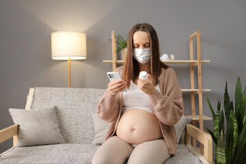 Sick displeased pregnant woman wearing medical mask sitting on sofa with medicine and smartphone...