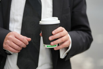 man dressed in a black suit and white shirt holding a recyclable glass. man holding a cup of coffee.