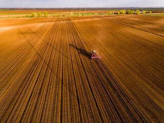 Aerial shot of a farmer seeding, sowing crops at field. Sowing is the process of planting seeds in...