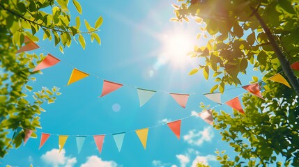colorful pennant string decoration in green tree foliage on blue sky summer party background