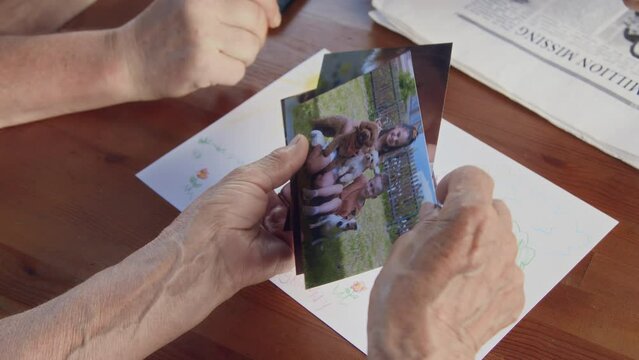 Close-up footage of hands of unrecognizable senior people sitting around table, looking at photos of young children and kids pencil drawing, while chatting at retirement home