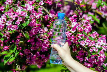  Girl holds a bottle of drinking water against the background of a blooming weigela

