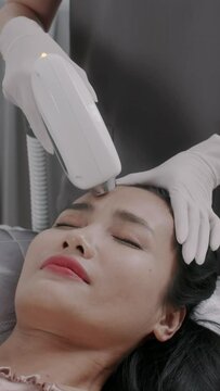 Vertical shot of cheerful female client having facial laser treatment when attending beauty center