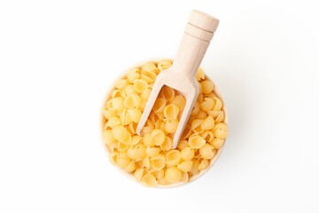 Shell shaped pasta in bowl with wooden scoop on white background. Top view