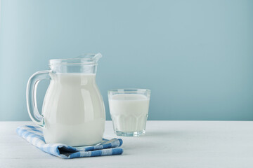 Milk in jug and glass on wooden table and blue background. Concept of farm dairy products, milk...