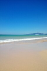 Atlantic ocean and beach with golden sand and blue sky in Tarifa, Spain. Playa de Bolonia on Atlantic coast of Tarifa, Province of Cadiz, Andalucia, southern Spain. Waves on Levante wind on summer day