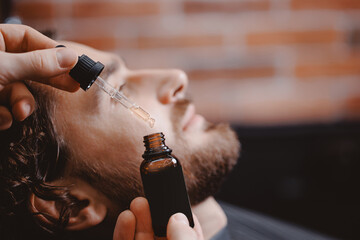 Young man holding pipette with oil for beard hair. Concept spa cosmetic and treatment wellness and...