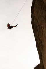 A woman is hanging from a rope on a cliff. Concept of adventure and excitement, as the woman is...