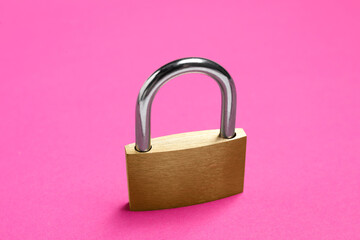 One locked steel padlock on pink background, closeup