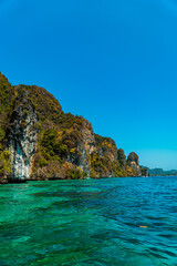 Fototapeta na wymiar Large rock cliffs covered with green trees face directly to the vast Andaman Sea. The view of rock cliffs and the ocean is an icon of tropical tourism on Phi-phi Island in Thailand