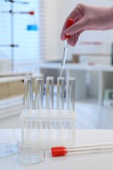Laboratory analysis. Woman dripping liquid into test tubes at white table indoors, closeup