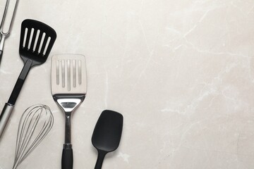 Different spatulas, whisk and carving fork on light marble table, flat lay. Space for text